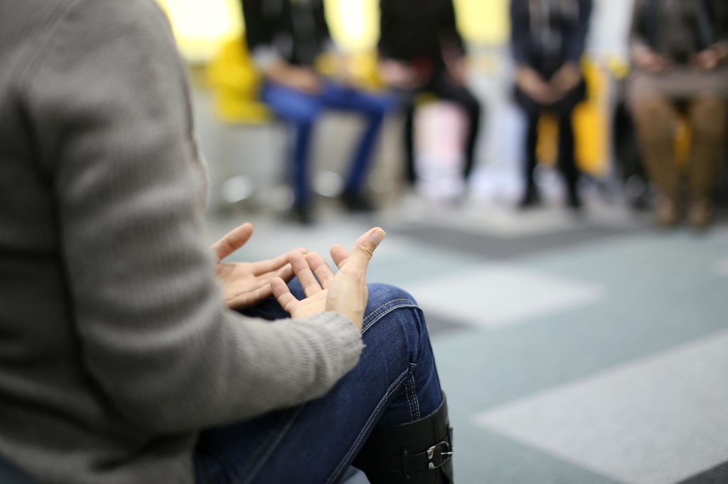 A seated person addresses others in a small group. Caption: Cognitive behavioral therapy is an evidence-based talk therapy that examines how an individual’s thoughts, behaviors, and emotions are connected.